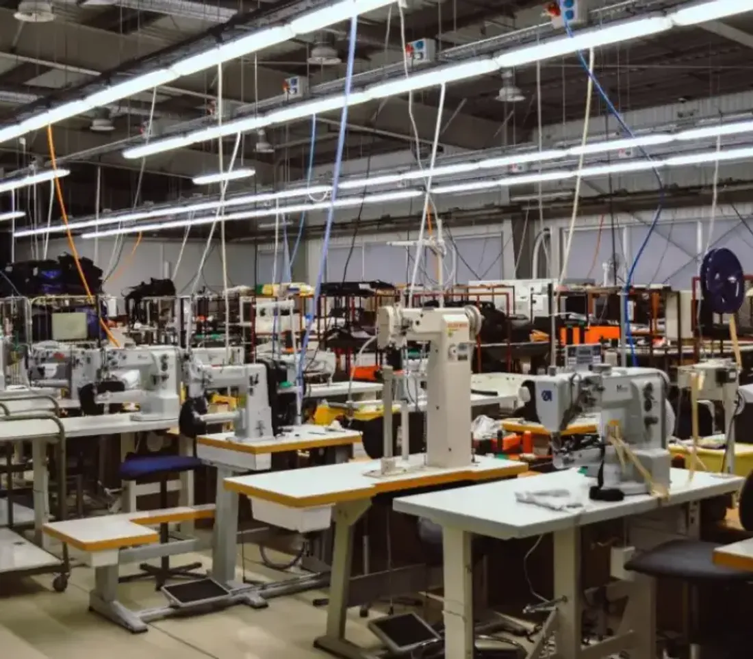 Rows of industrial sewing machines under strip lighting on the LeelineBags production floor