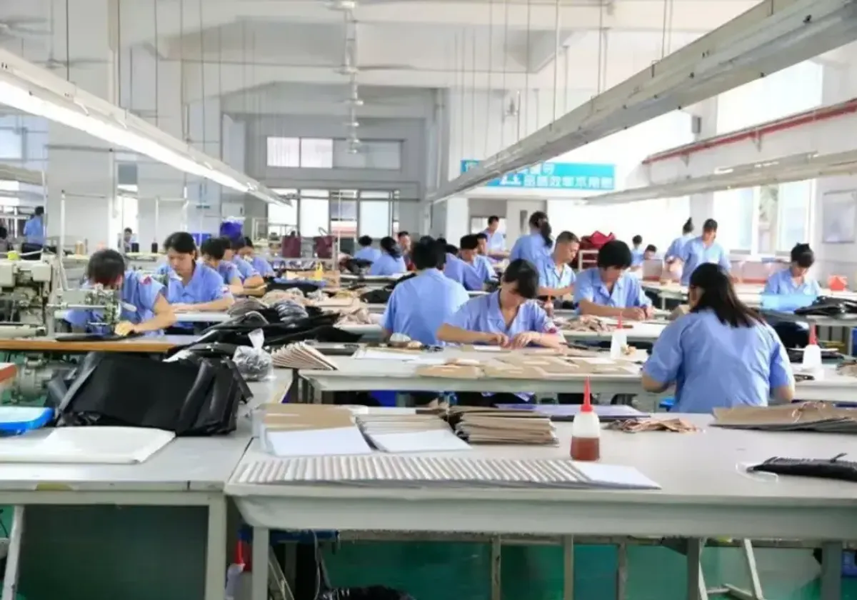 A row of industrial sewing machines on the LeelineBags production floor, a stitcher working at the nearest