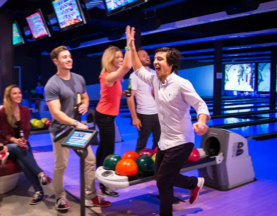 A group of colleagues celebrating a strike on a lane, one raising a hand for a high-five