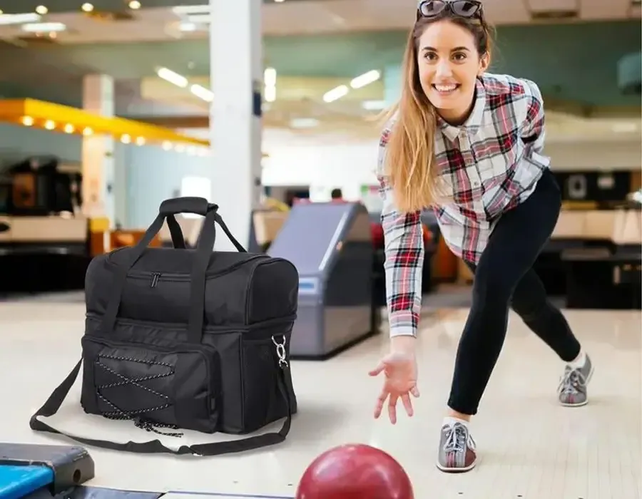 A bowler crouched at the foul line mid-delivery with a black ball bag standing open on the lane behind her
