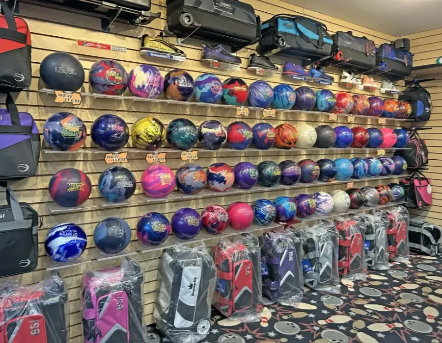 A pro-shop wall shelved with rows of bowling balls and bags displayed on hooks above them