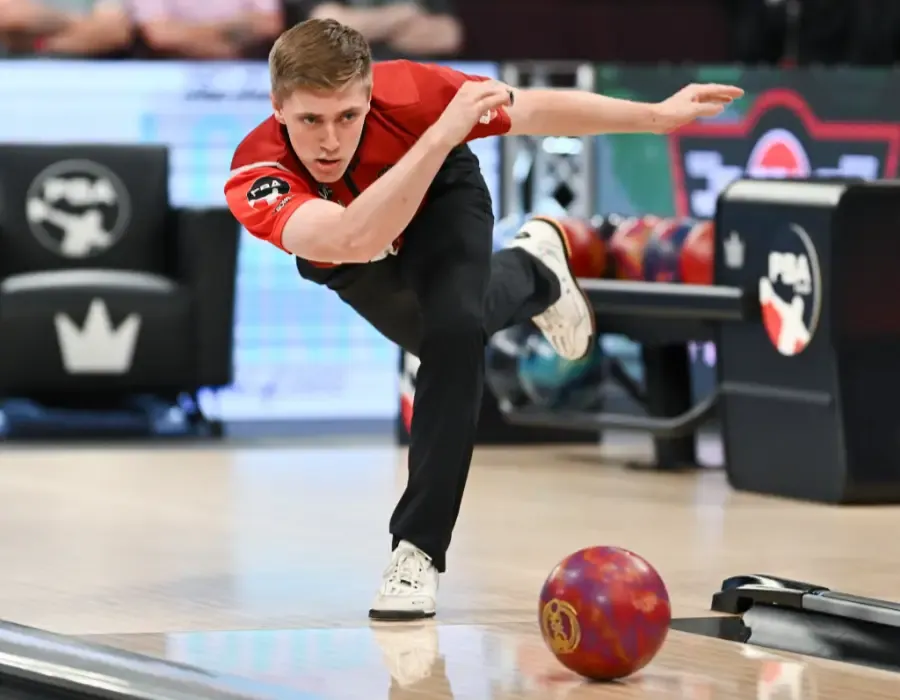 A professional bowler mid-delivery on a tour lane, arm extended, a ball travelling down the lane ahead of him