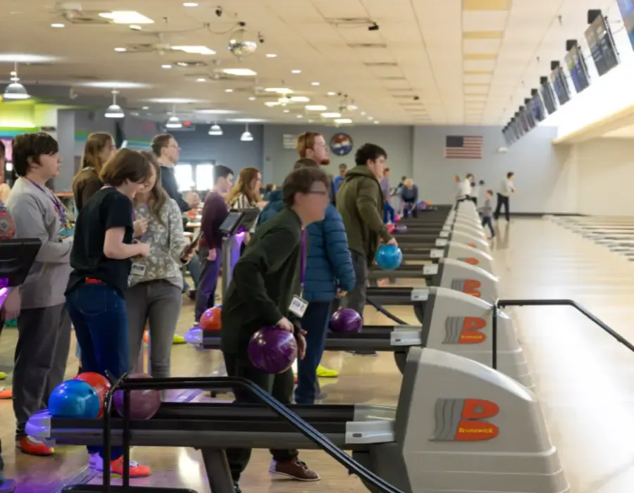 A bowling centre concourse with a row of lanes, ball racks and players lined up to bowl
