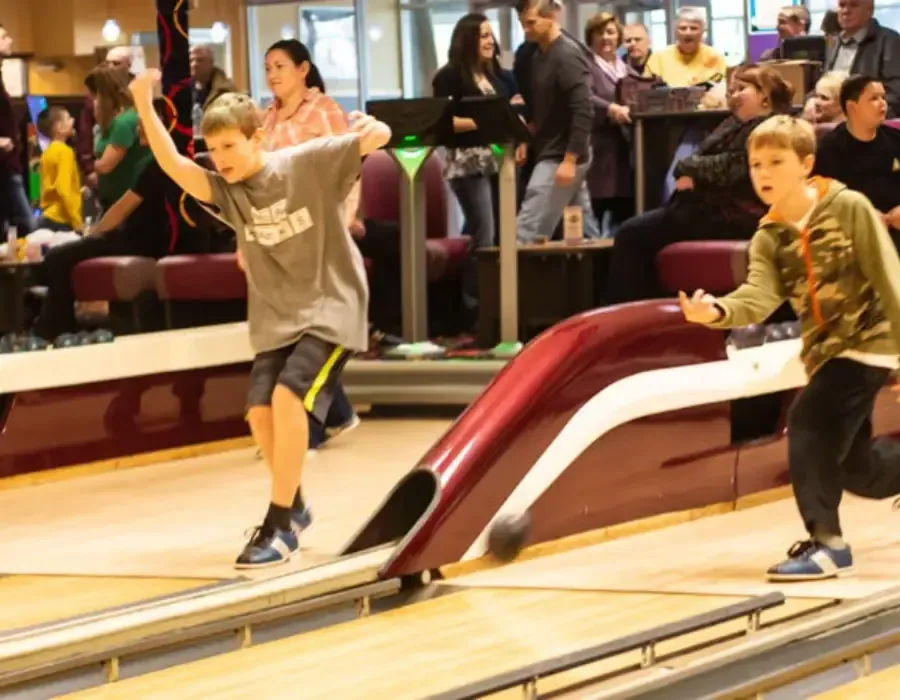 Two children mid-throw on adjacent lanes with a crowd of spectators behind them