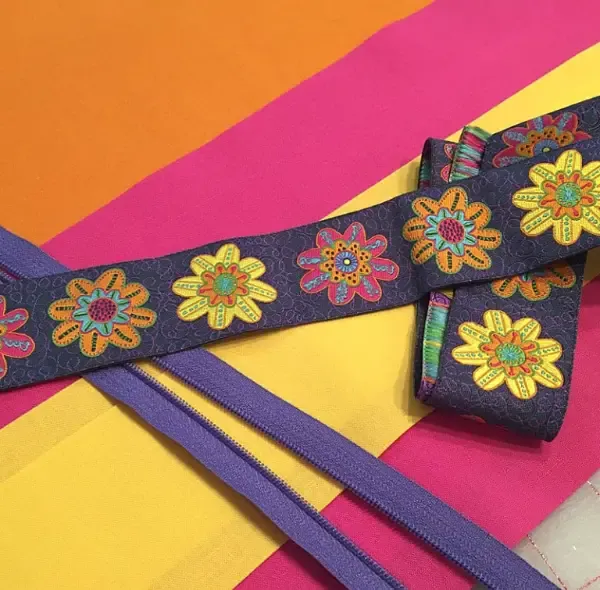 A strip of embroidered floral webbing with zips laid across a yellow and pink ground