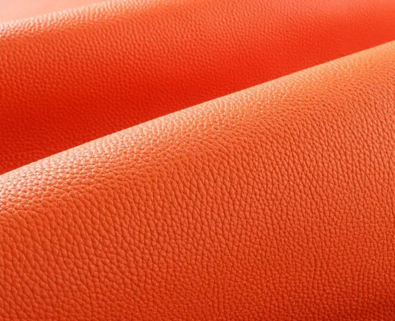 A close view of two folds of orange full-grain leather, the grain catching the light