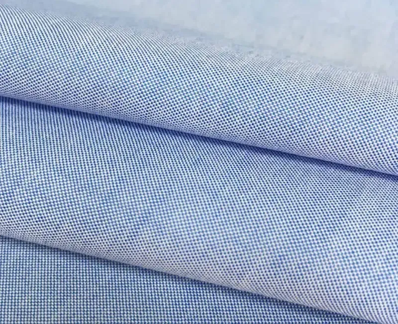A close view of folded light-blue oxford cloth, the fine weave running across the frame