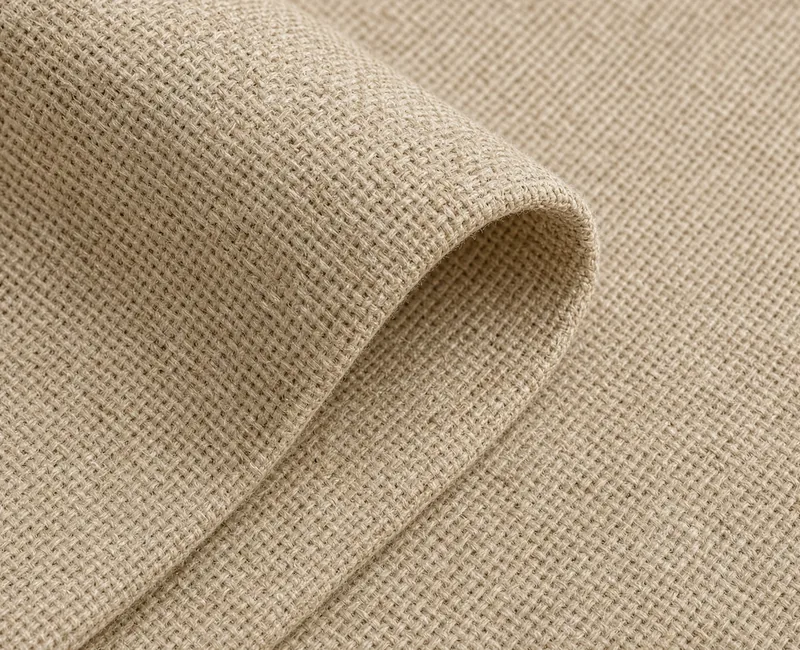 A close view of a fold in natural beige recycled woven cloth, the heavy weave and a soft edge filling the frame