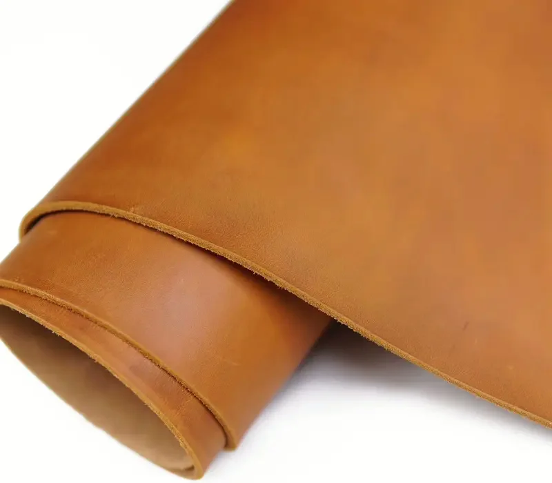 A length of tan full-grain leather rolled into a soft cylinder, catching warm light against a dark background