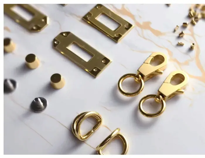 Anchor plates, keeper loops and swivel snap hooks in polished gold with a few gunmetal studs, laid out on a pale marble surface