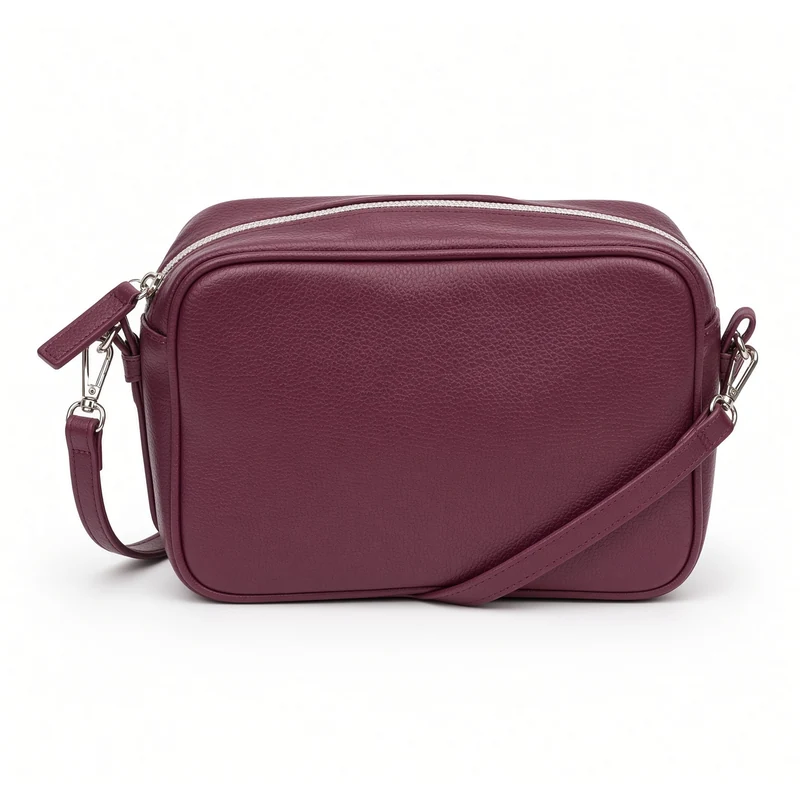 A plum grained-leather camera crossbody bag with a full-width zip and white piping, its strap clipped to a side D-ring