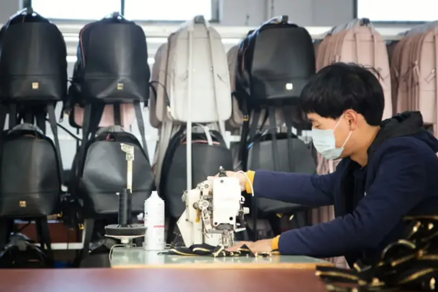 A finisher turning a finished black bag to check its hardware against a row of completed bags on a rack