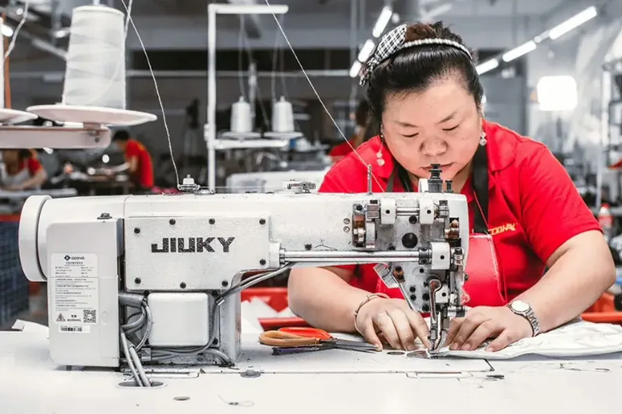 A machinist binding a bag panel at an industrial flat-bed sewing machine on the production line