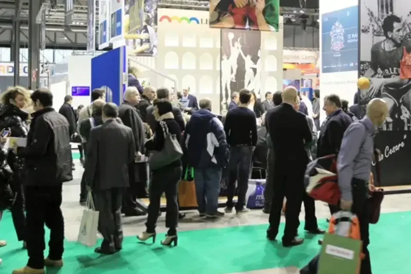Visitors walking a trade-show floor carrying branded bags between exhibition stands