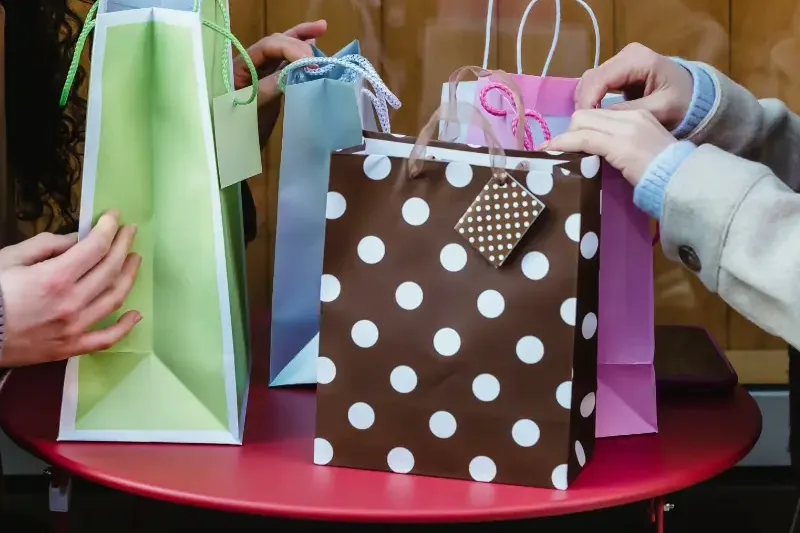 Hands folding tissue and dropping gift bags and boxes into a presentation package on a table