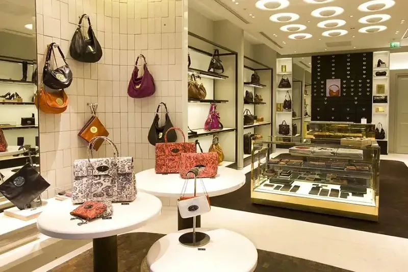 A bag boutique interior with handbags and small leather goods displayed on lit plinths and shelves