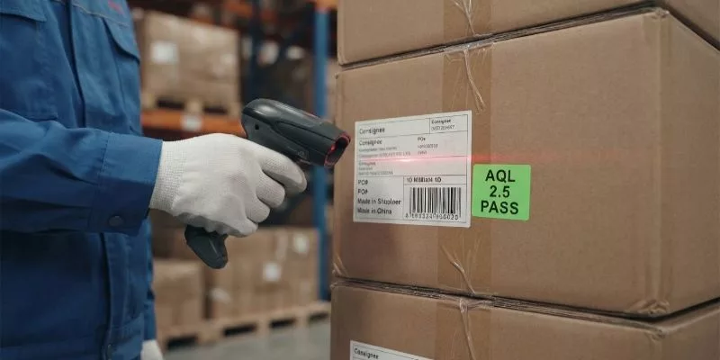 .Warehouse worker scanning an export carton with an AQL 2.5 Pass sticker.