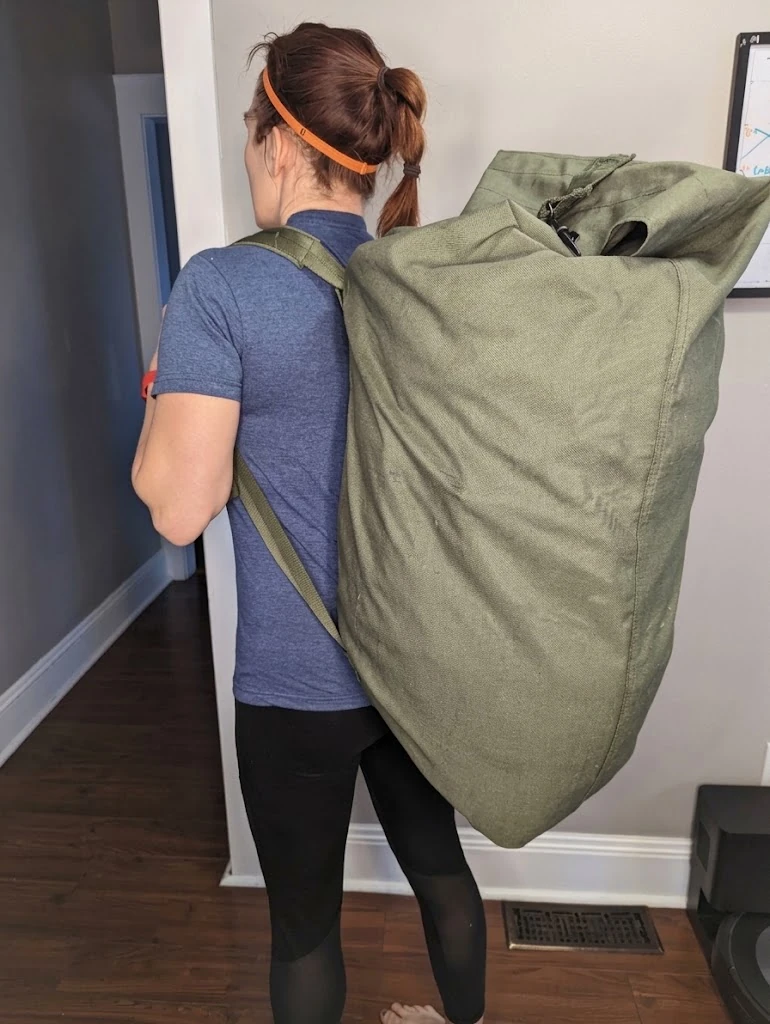 An olive rolltop duffle worn as a backpack to the shoulder inside a hallway