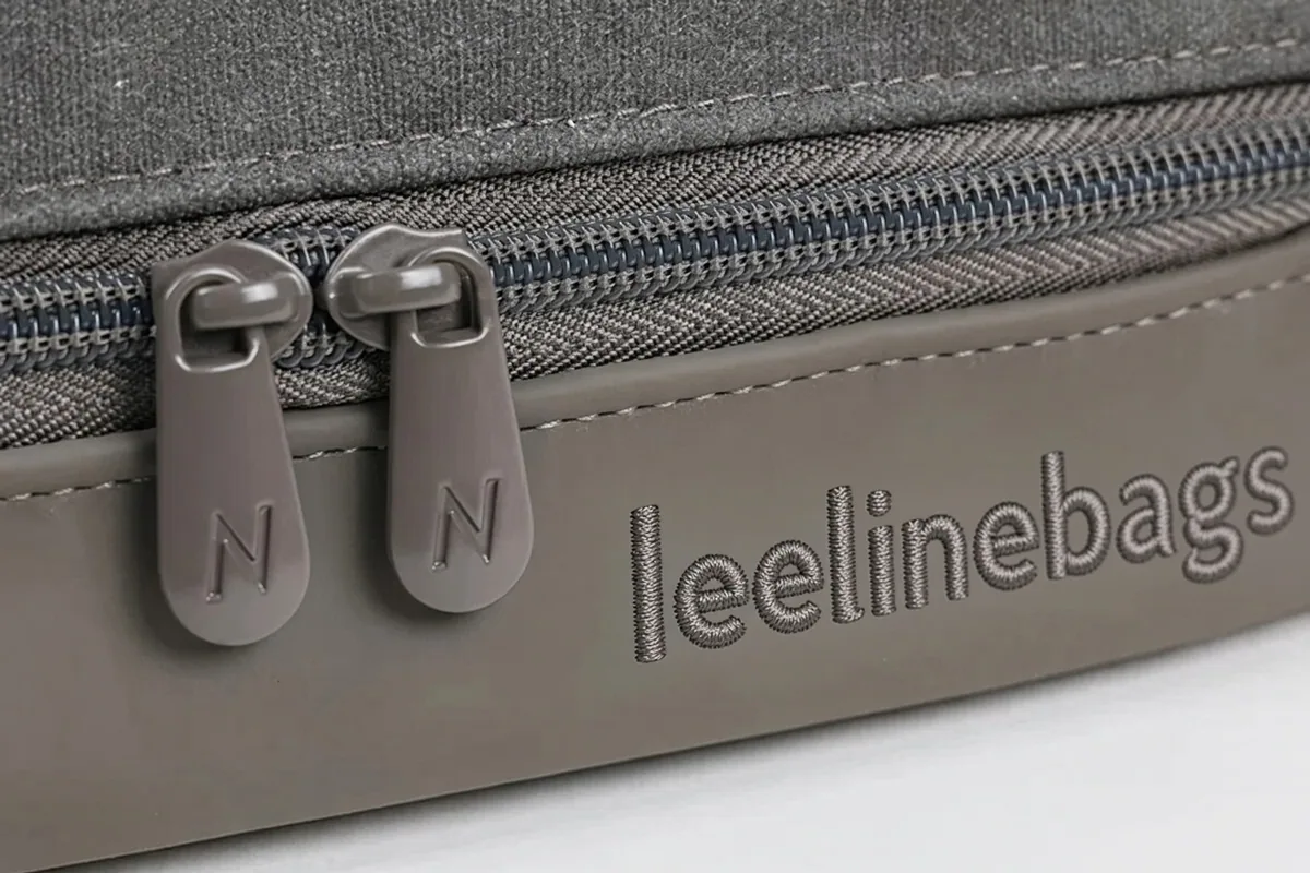 Two custom zipper pulls, each carrying a raised N, set above a leelinebags wordmark on a grey bag