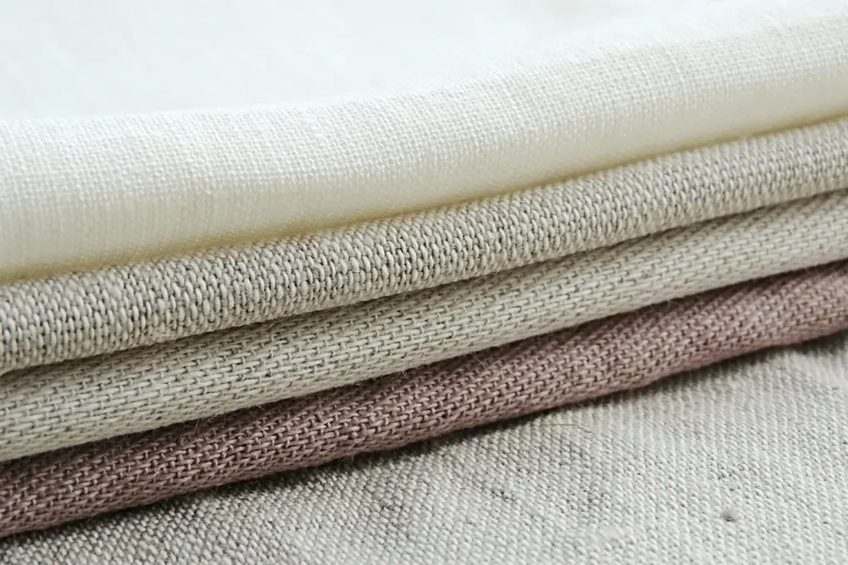 Folded lengths of linen in cream, taupe and grey showing its slub weave