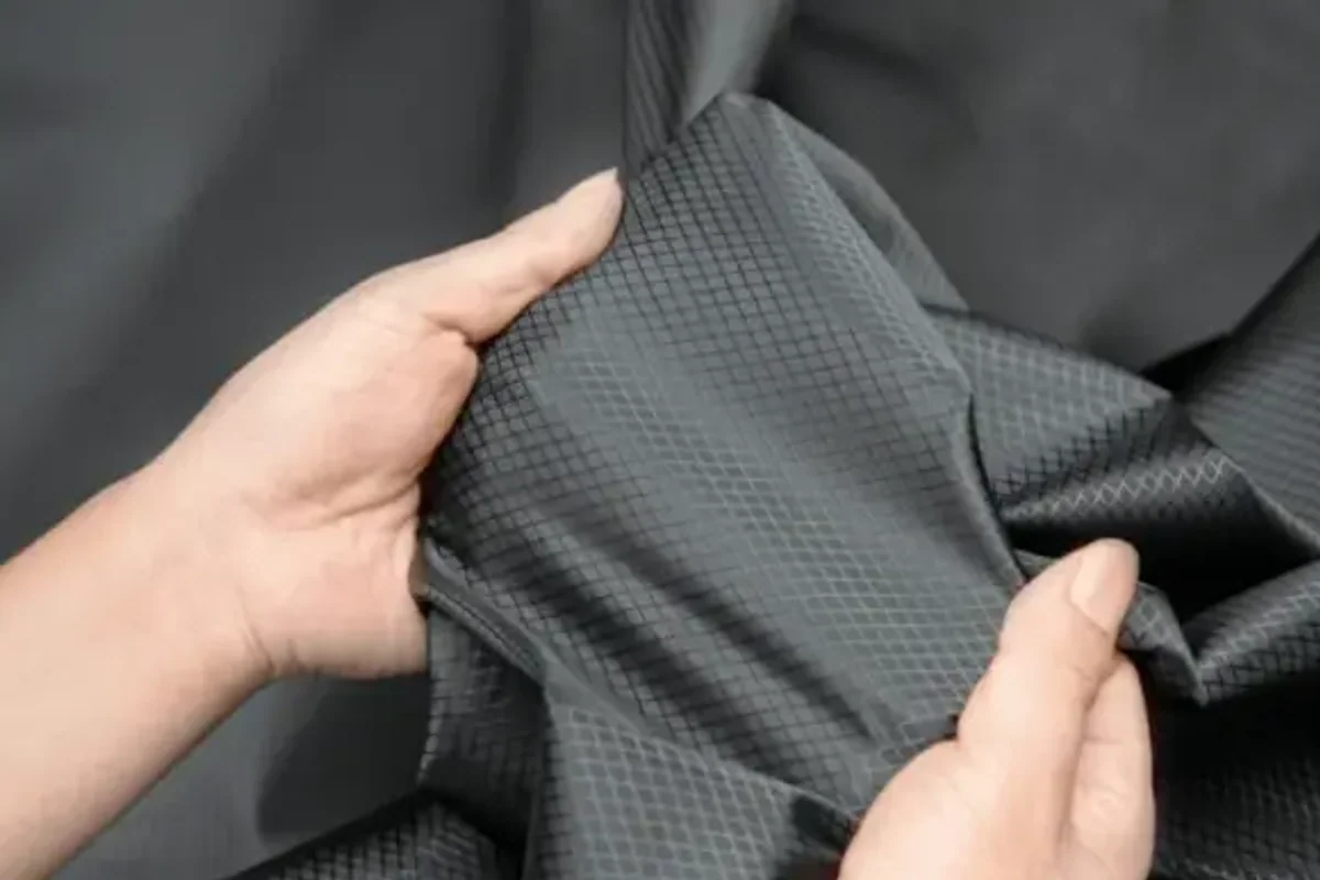A hand creasing a swatch of dark grey polyester fabric