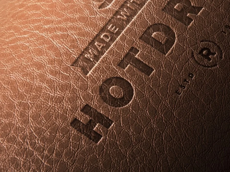 A debossed logo pressed into the pebble grain of a tan leather handbag panel