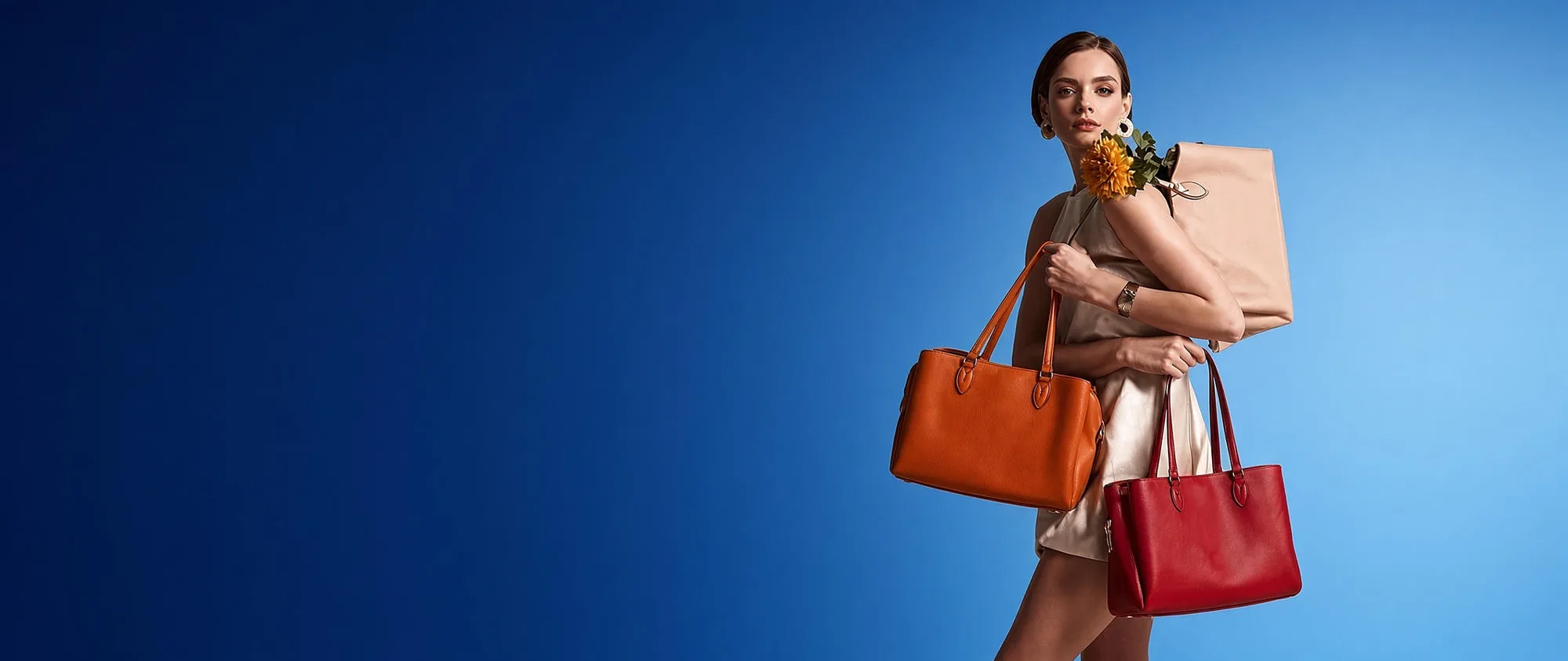 A model carrying three custom handbags — an orange leather tote, a red leather tote and a tan shoulder bag — against a blue studio backdrop