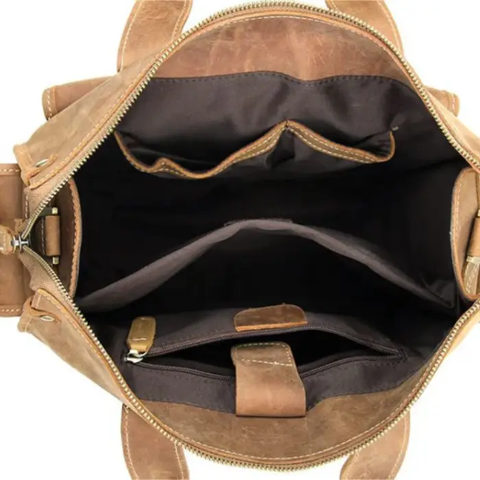 The open interior of a tan leather bag showing a dark lining, a zip pocket and a slip divider