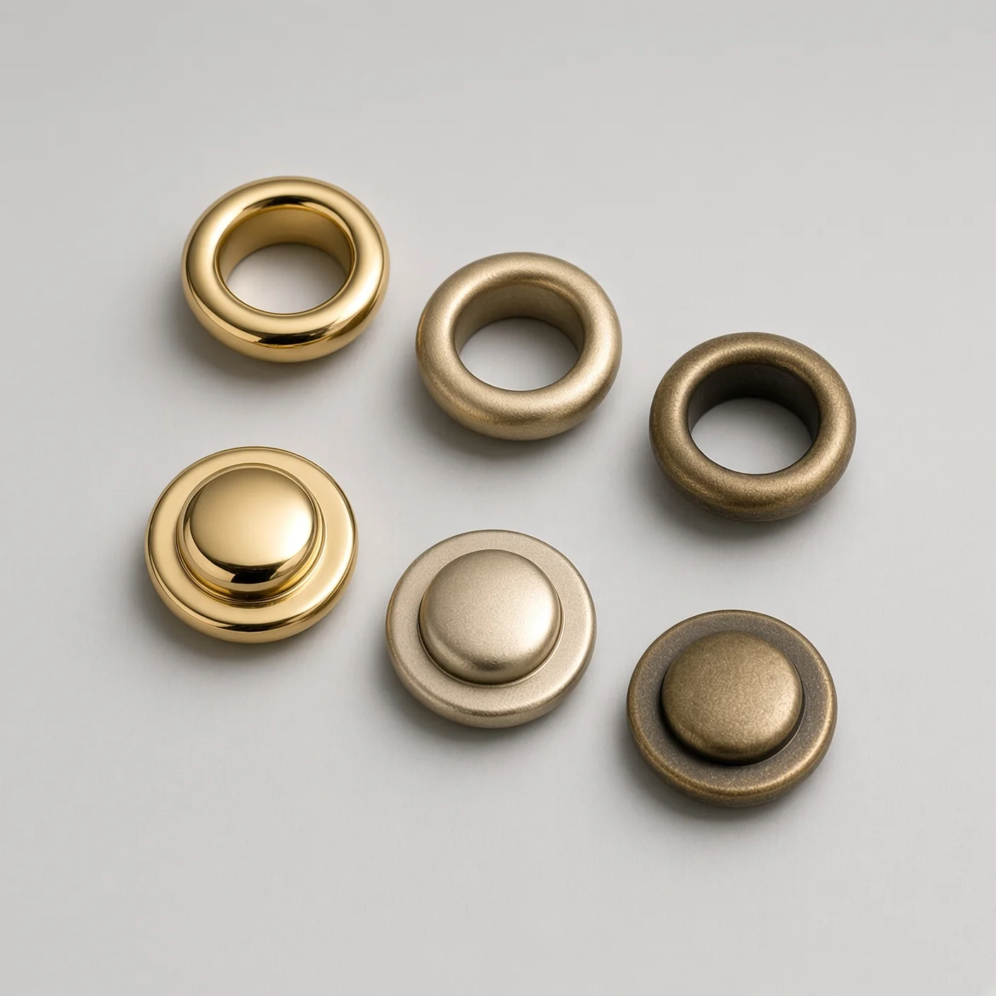 Six gold-toned bag fittings on a light grey ground — eyelets on the top row and snap buttons below, each row running from mirror-polished gold through satin to antique bronze