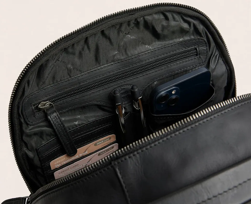 The opened interior of a black backpack showing the technical nylon lining, a zip pocket and an organiser panel with pen loops, a phone slot and card sleeves