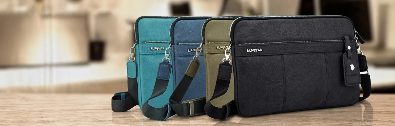 Four messenger bags in teal, blue, olive and black standing in a row on a table