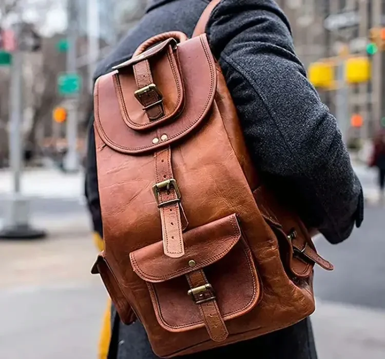 A person in a coat on a city street carrying a tan leather backpack with buckled straps