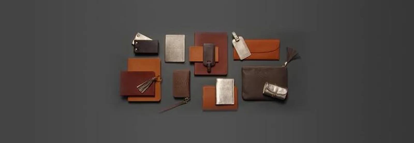 A flat-lay of tan leather wallets, card holders and small goods on a dark surface