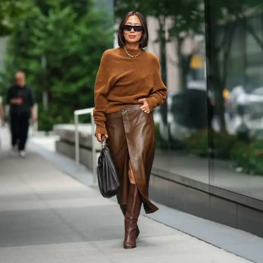 A model in a brown leather skirt and knee-high leather boots holding a black leather bag