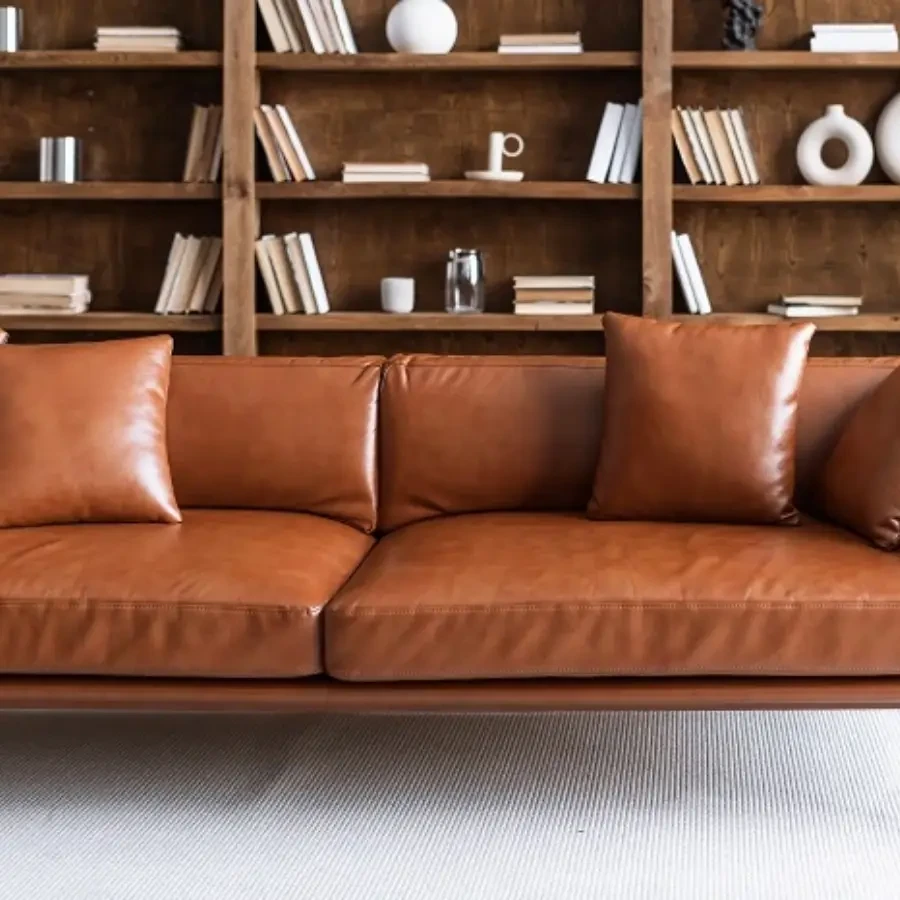 A tan leather sofa with matching cushions in front of a wooden bookshelf