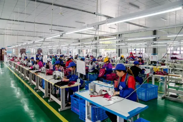 A wide production hall of sewing operators at rows of machines stitching pink bags under strip lighting