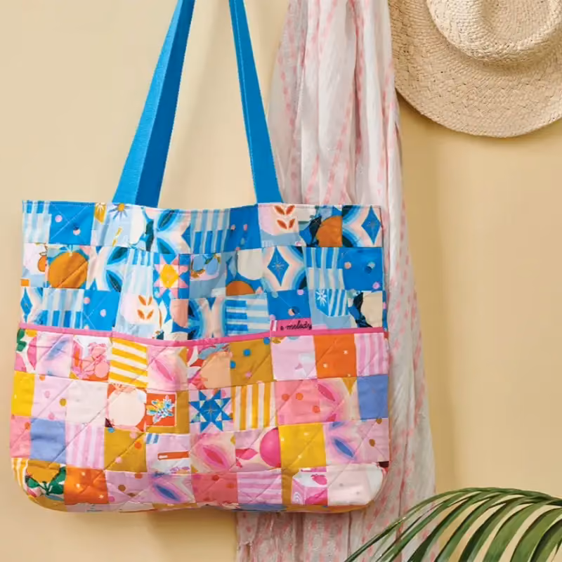 A pieced patchwork quilted tote hanging against a wall, showing the pattern across the face
