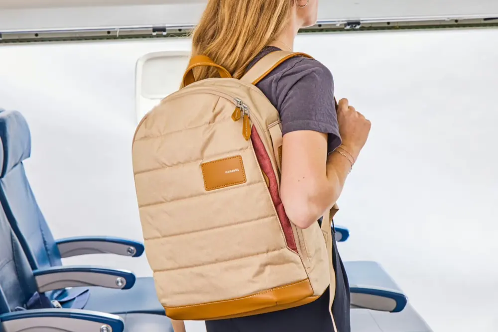 A commuter wearing a tan quilted backpack while boarding a flight