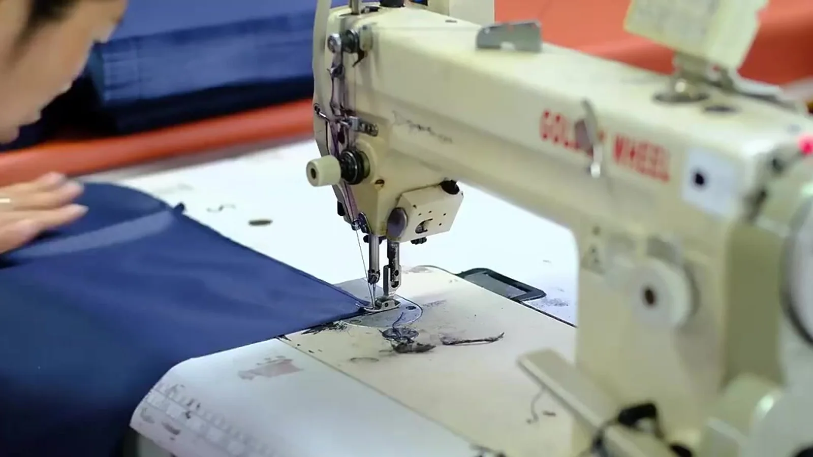 A stitcher guiding navy fabric under the needle of a sewing machine on the LeelineBags line — the film's opening frame