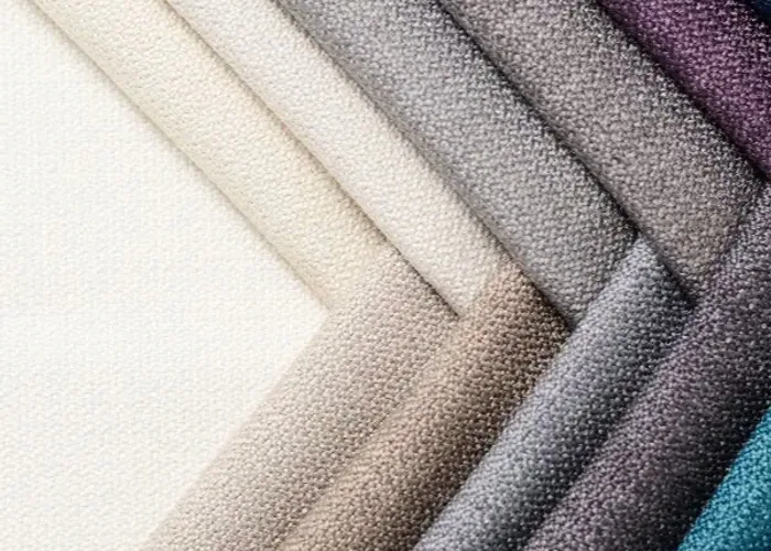 Four folded school-bag shell fabrics in cream, grey, black and blue, laid side by side at close range