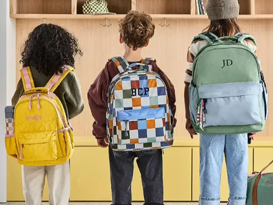 Young students standing in a row from behind, carrying small backpacks in bright prints and colours