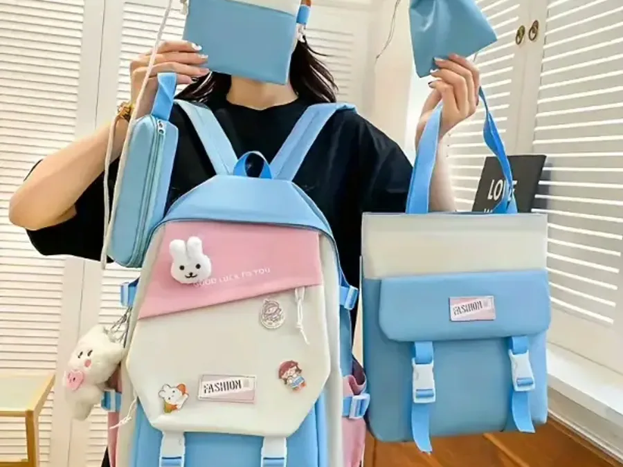 Two pastel school backpacks with a plush charm held up side by side against a classroom wall