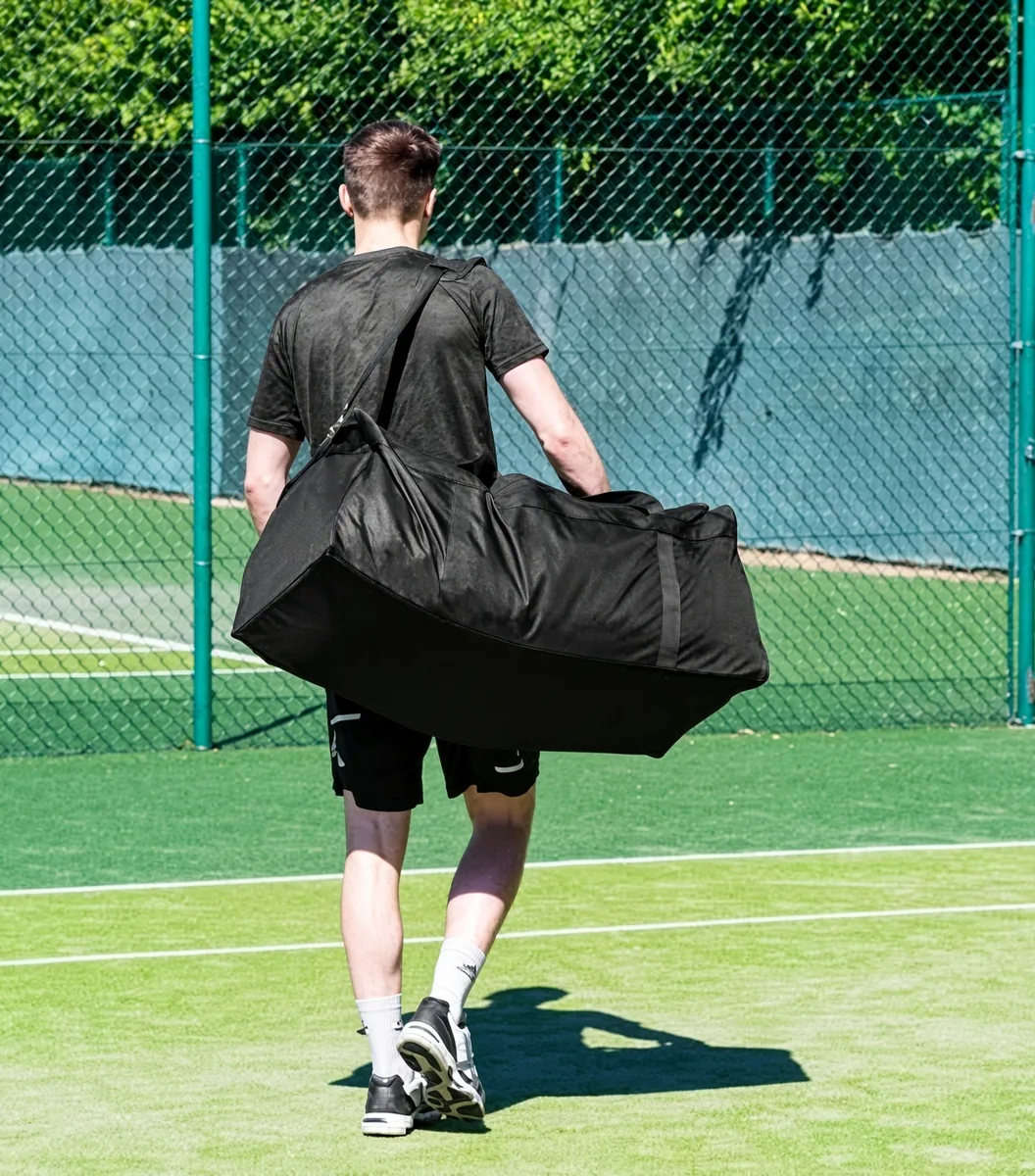 A tennis player walking off a floodlit court carrying a kit duffle