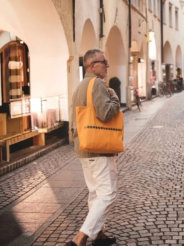 An orange canvas tote carried along a stone arcade at dusk