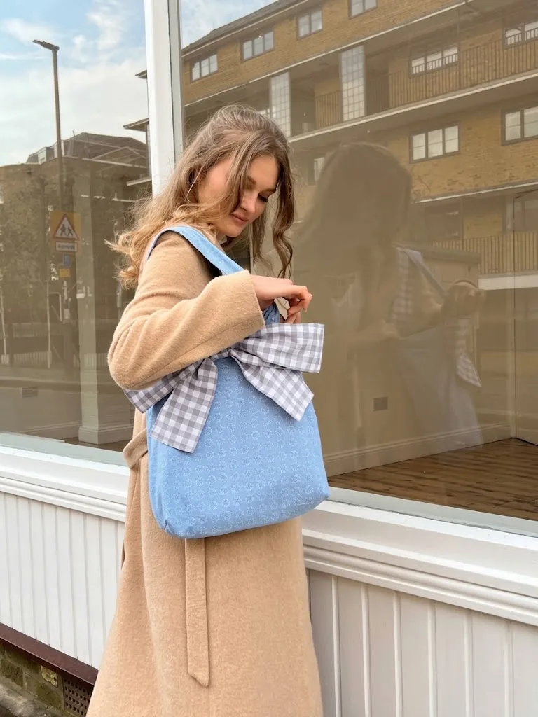 A blue bow-detail tote held in front of a shop window