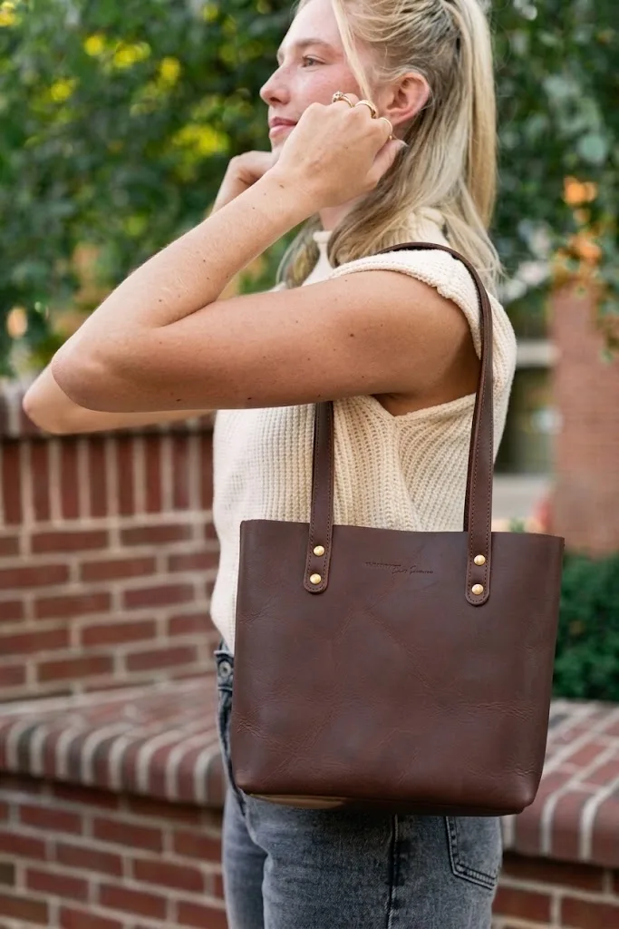 A brown leather tote carried against a low brick wall