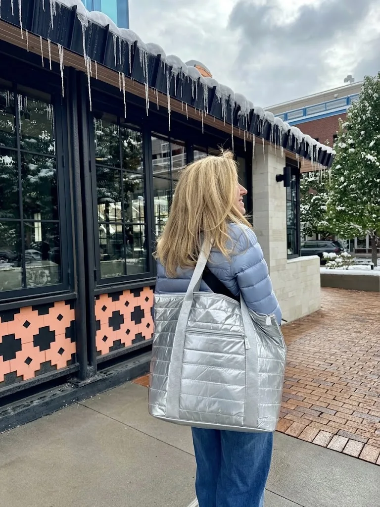 A large silver quilted tote carried past a shopfront on a winter street