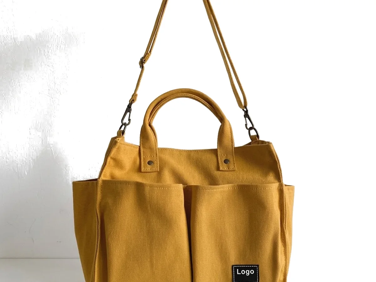 A mustard cotton canvas tote travel bag with a blank label patch on a plain ground