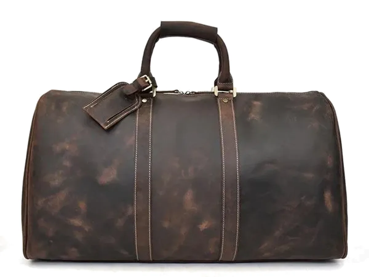 A brown leather barrel travel duffel with a luggage tag on a plain ground