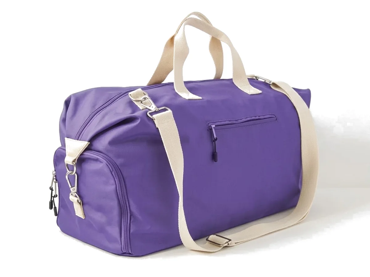 A purple nylon travel duffel with webbing handles on a plain ground